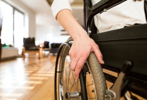 Unrecognizable young disabled woman in wheelchair at the at home in her living room. Close up of her arm laid on wheel. S